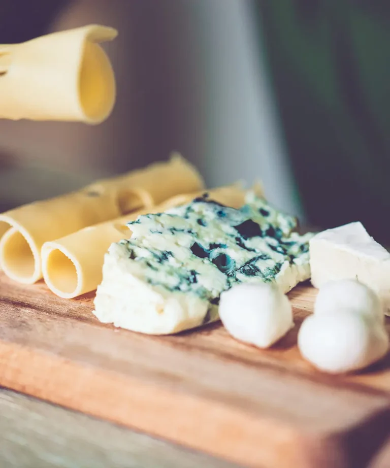 Assorted cheeses on a wooden board — rolled cheese slices, blue cheese, mozzarella balls and white cheese cubes
